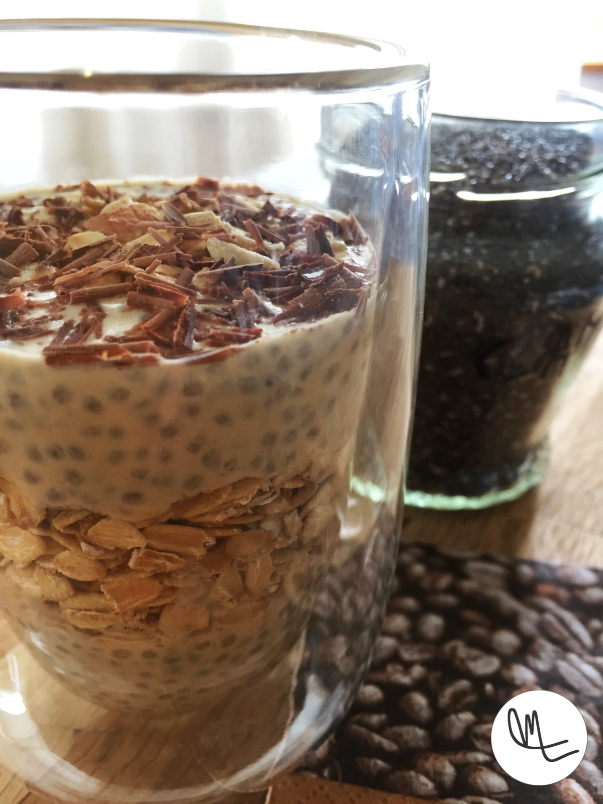 Glass with chia pudding with a layer of oats, topped with chocolate flakes, with a background of chia seeds and a napkin as a liner.